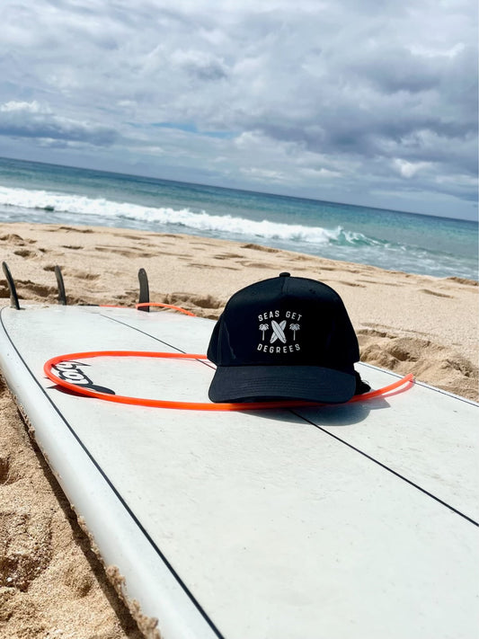 Retro Rider Snapback lifestyle shot with surfboard in black — Seas Get Degrees