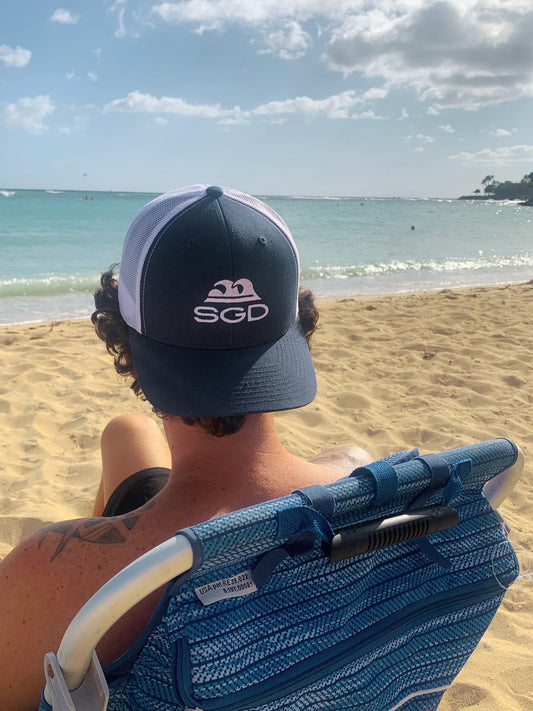 Blue Tide SGD Trucker Hat worn backwards at beach sunset — Seas Get Degrees lifestyle