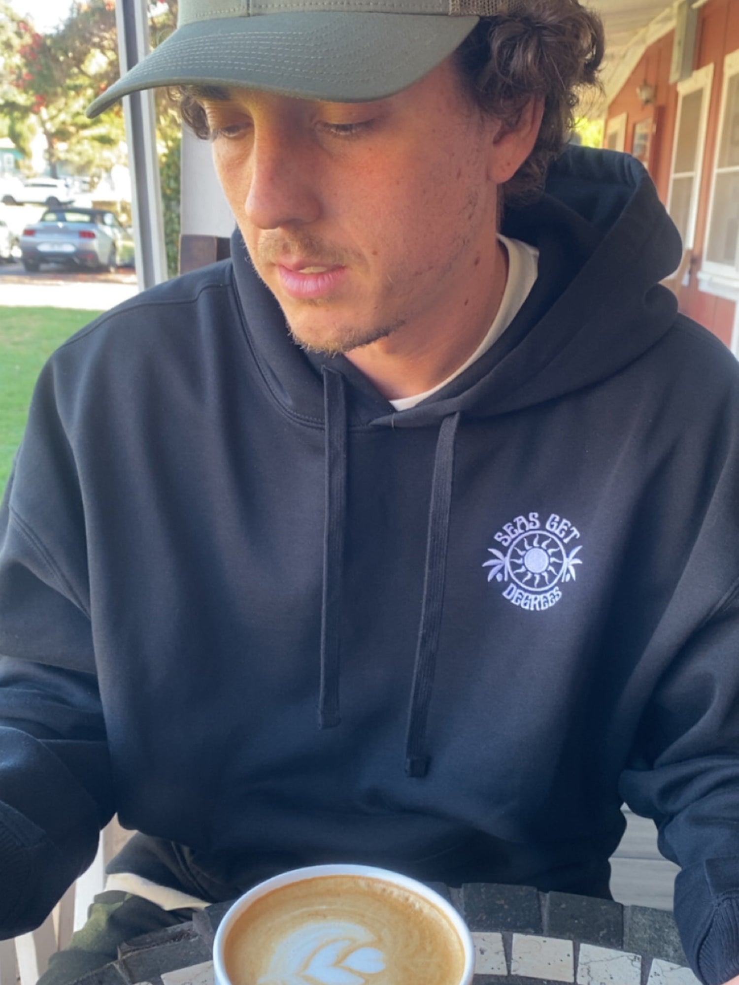 Chase the Sun Oversized Embroidered Hoodie lifestyle shot at coffee cafe — Seas Get Degrees