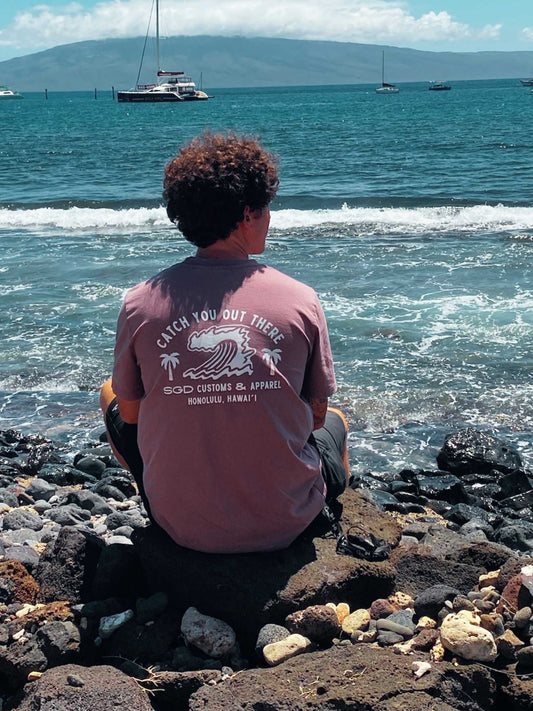 Model wearing Endless Wave Tee in kaffa coffee sitting on rocks overlooking the ocean in Hawaii — Seas Get Degrees coastal lifestyle